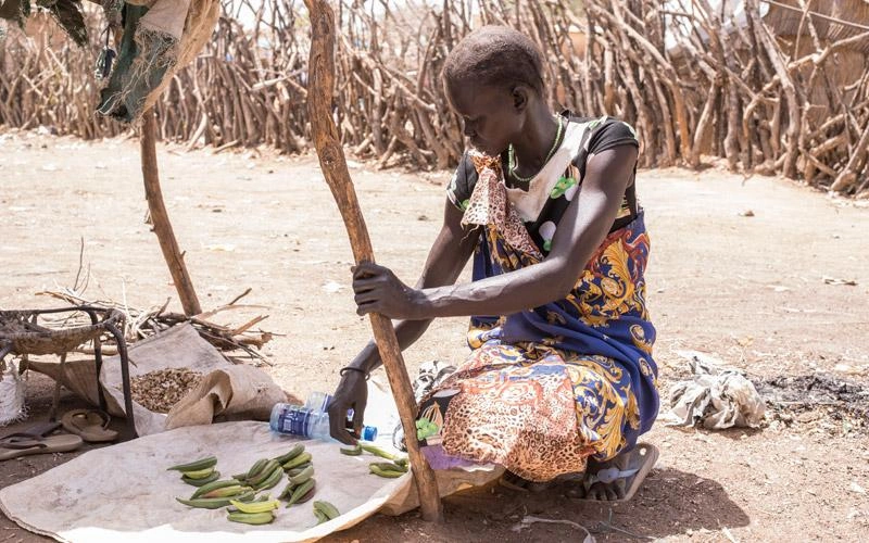Une mère sud-soudanaise étale ses récoltes sur une natte, à l'ombre d'un appentis.