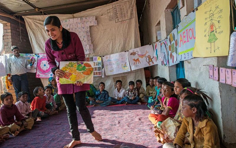 Une fillette indienne tient un livre ouvert devant un groupe d’enfants rassemblés en cercle.