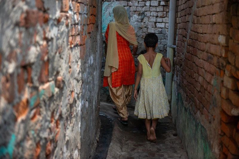 Une femme et une jeune fille marchent dans une ruelle, s’éloignant de la caméra.