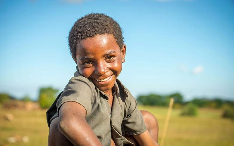 En Zambie, une jeune fille est accroupie, un grand sourire illuminant son visage.