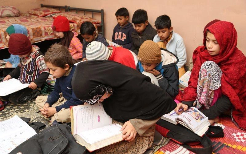 Un groupe d'enfants est assis par terre, tous penchés sur leurs manuels scolaires.
