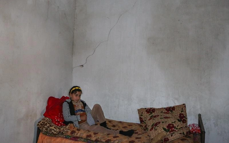 Une jeune fille est assise sur un lit dans une pièce en béton.