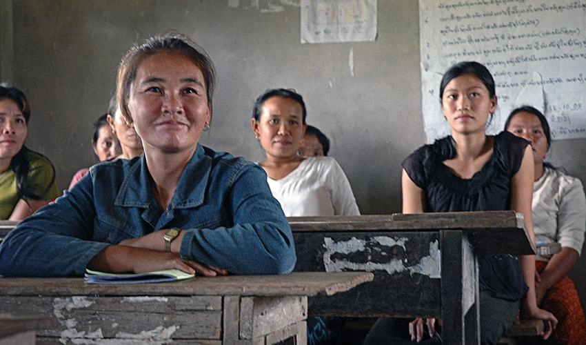 Dans une salle de classe au Laos, des mères sont assises à des pupitres et regardent vers l'avant de la salle.
