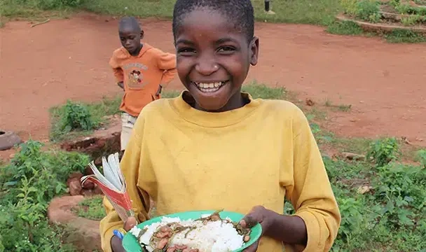 A schoolboy smiling while holding a plate of food.