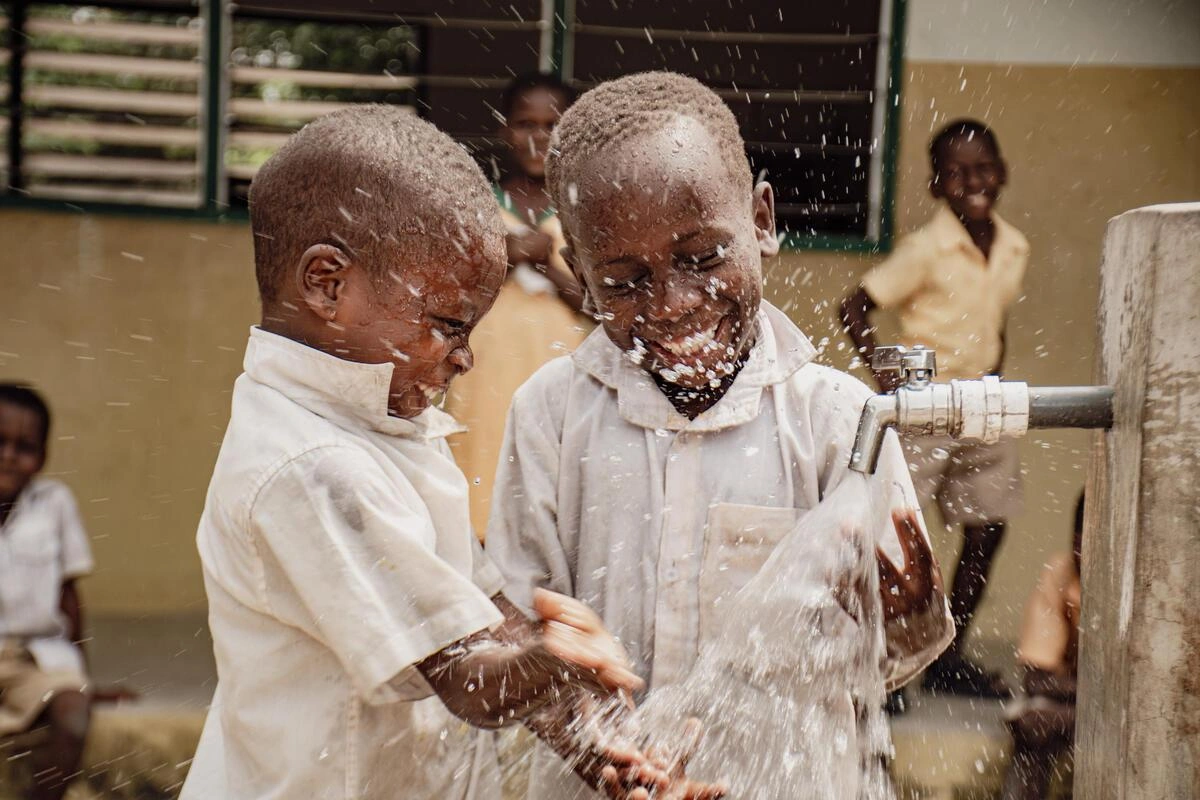 Deux enfants jouent avec de l'eau propre et fraîche provenant d'un point d'accès public à l'eau en plein air.