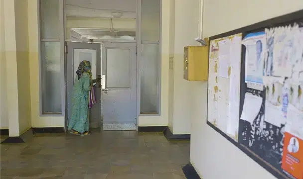 A women holding a bag, begins to open a door at the far end of the room.