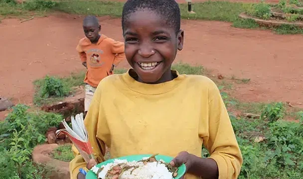 A boy from Burundi cheerfully holds a plate of nutritious food.
