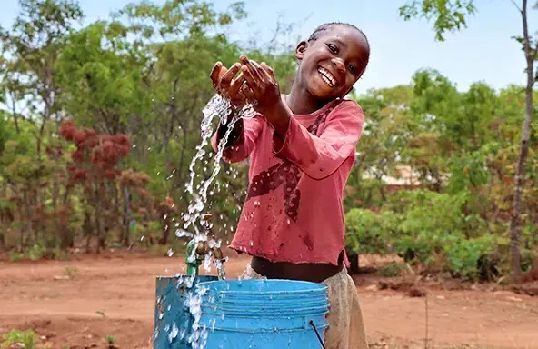 Une fillette vêtue d’un chandail rouge joue avec l’eau qu’elle a tirée du robinet.