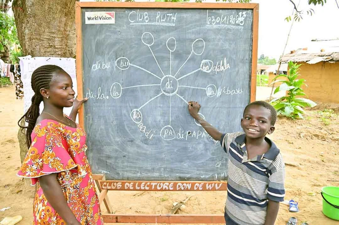 Junior sourit en montrant du doigt ce qu’il apprend sur le tableau noir.