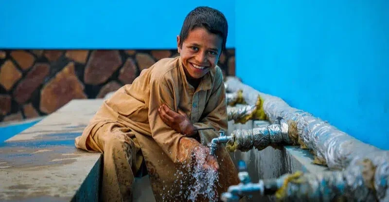 Un garçon sourit tandis qu’il va chercher de l’eau à un point d’eau public.