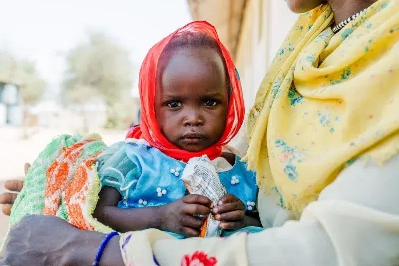 Une petite fille mange de la nourriture d'urgence contenue dans un sachet prêt à l'emploi.