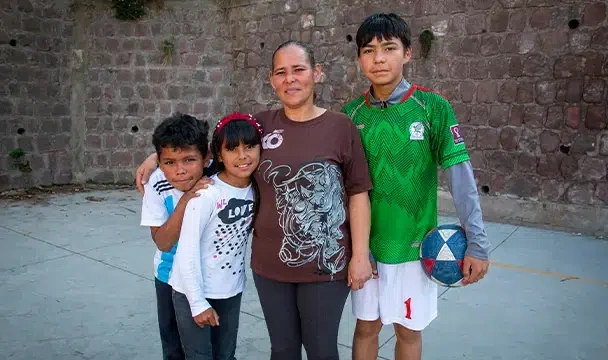 Mother Rosa stands with her three children in front of a stone wall. (Ecuador, 2022)