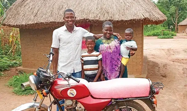 Family of four stands behind a red motorcycle outside their home in South Sudan.