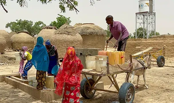 Un groupe de personnes remplissant des seaux d’eau potable à partir d’un point d’eau communautaire. (Niger, 2023)