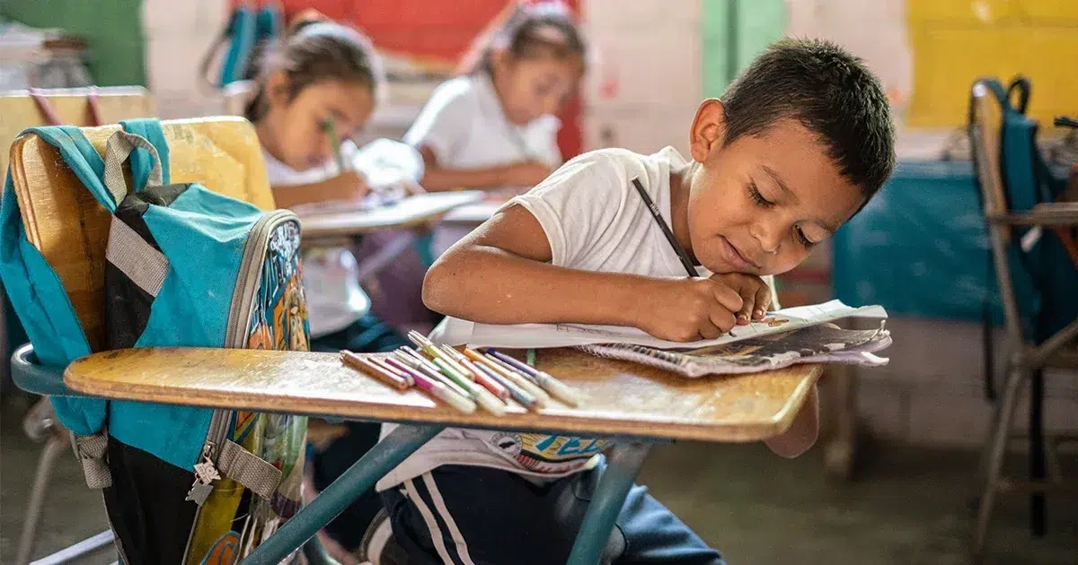 Un jeune garçon assis sur sa chaise, en train de dessiner sur une feuille de papier.