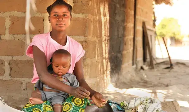 A deaf young woman in a pink shirt, sits, holding small a child.