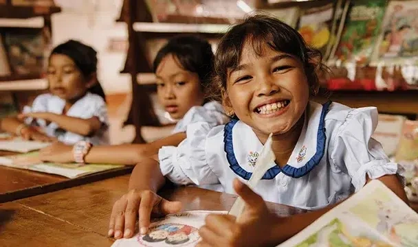Three girls wearing school uniform are in a library reading books.