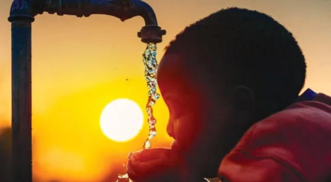 Child drinks from a public outdoor water point at sunset.