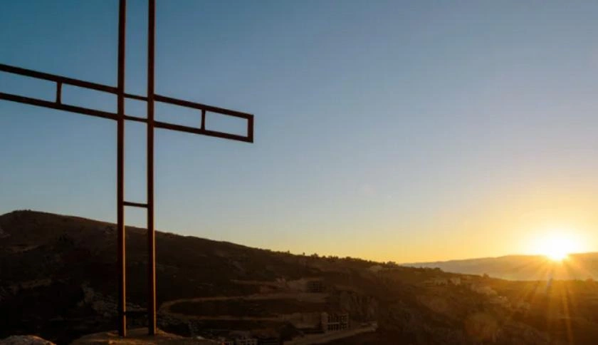 A large metal cross stands on a landscape with the golden tones of the sunset shining on it.