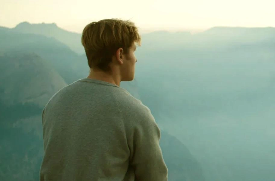 Man sitting on the edge of a cavern looking out across the expanse.