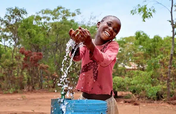 A girl wearing a red blouse is playing with the water she collected from the tap.