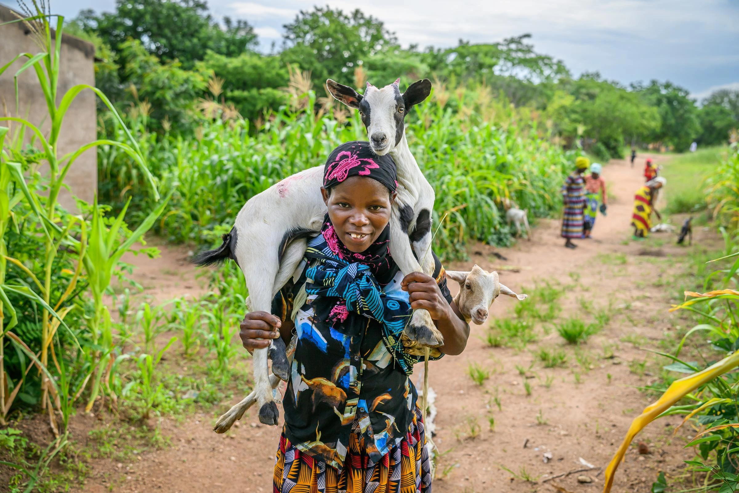 A happy woman carries goats on her back and on her shoulders.