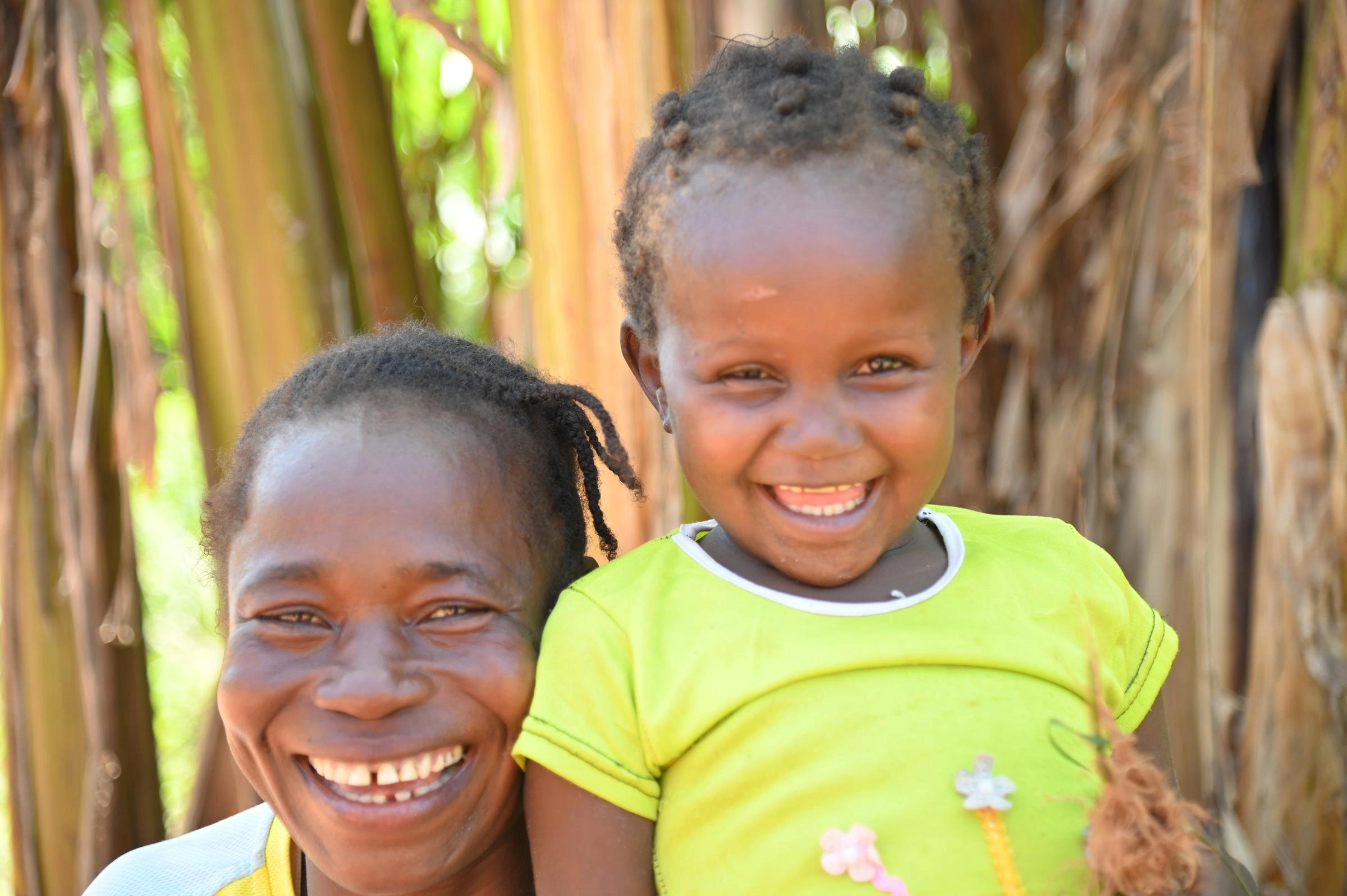A little girl smiles as she holds her grass doll beside her smiling mother.