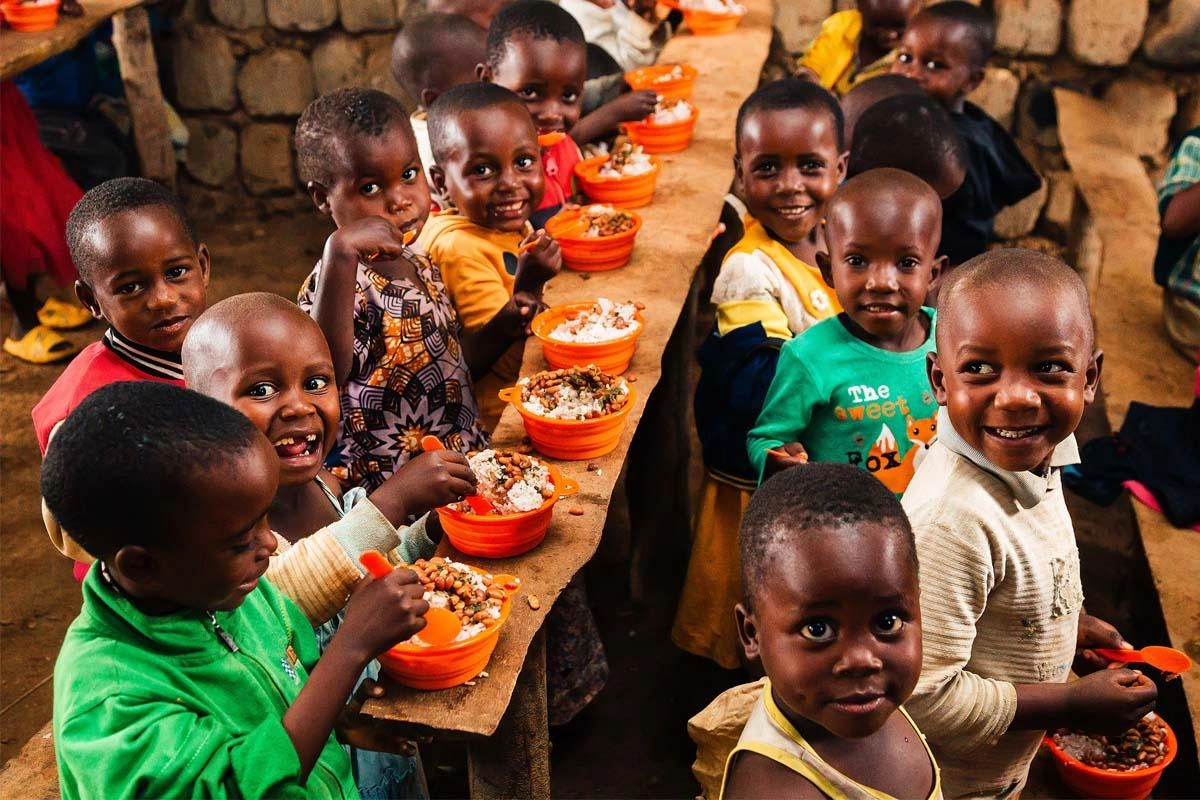 A group of children are eating from their orange bowls provided by World Vision.