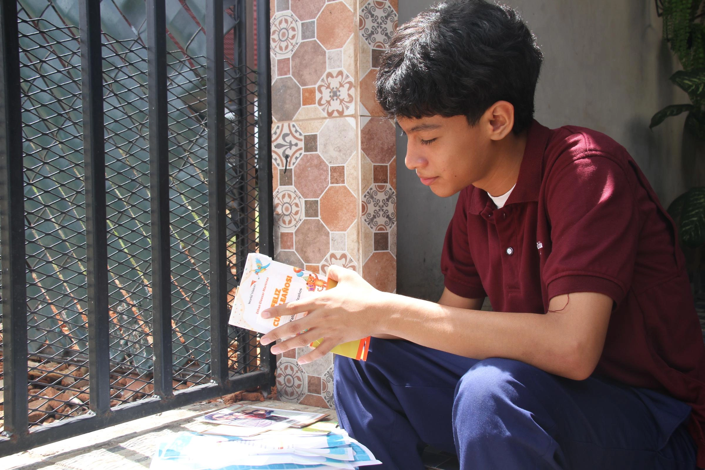 A young boy reads letters from his sponsor while sitting by a window.