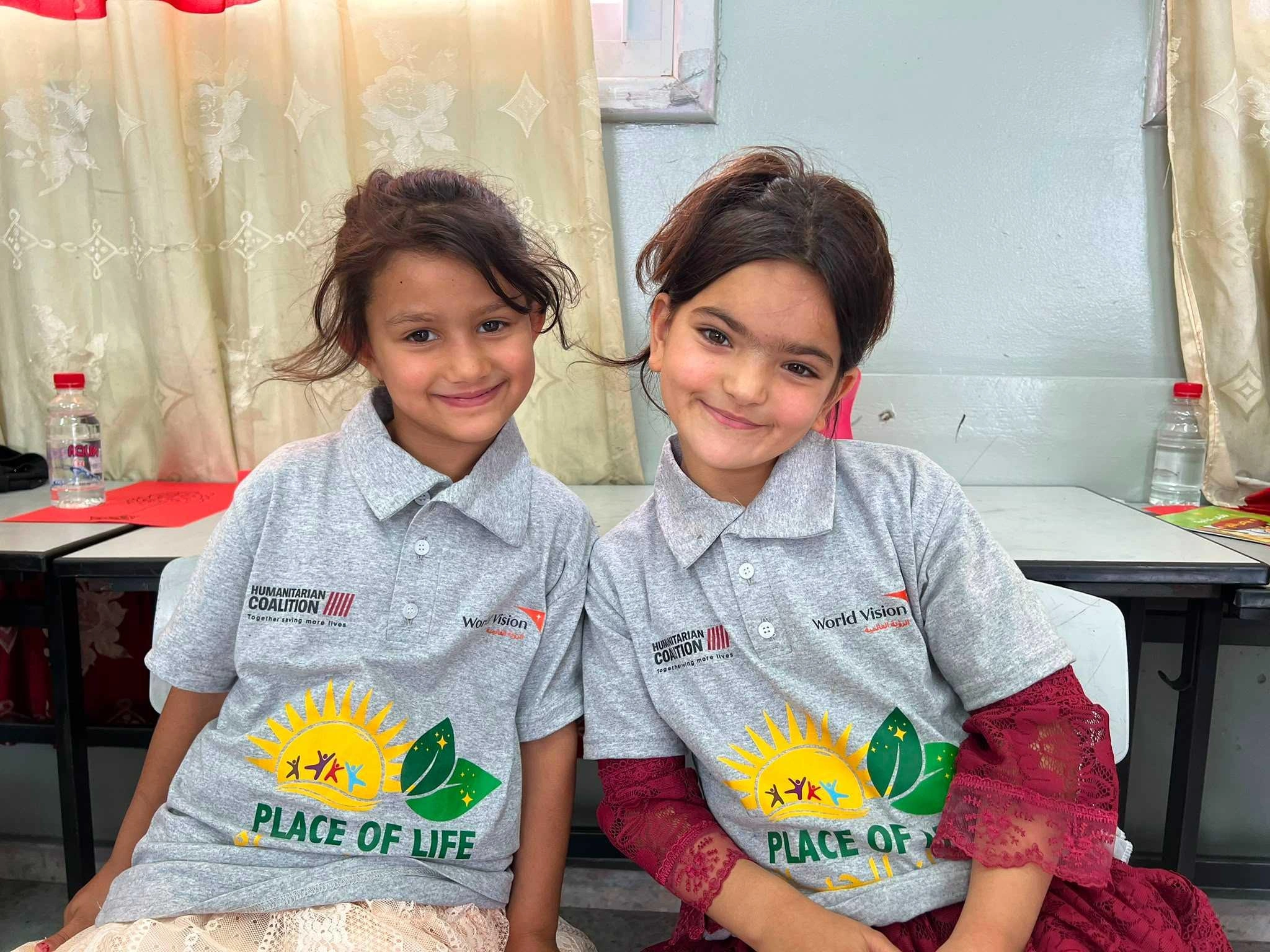 Two children wearing matching shirts smile.