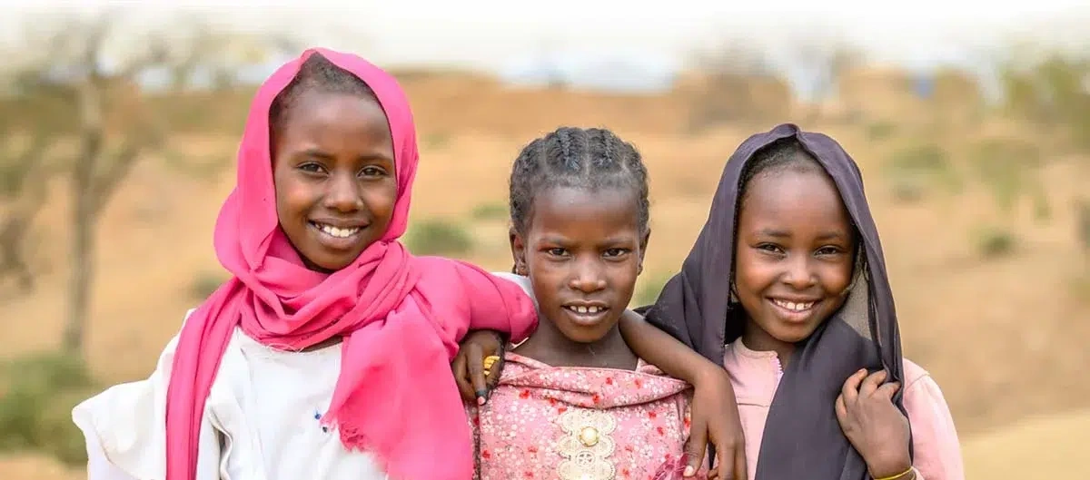 Three girls stand together with hope outside in Africa.