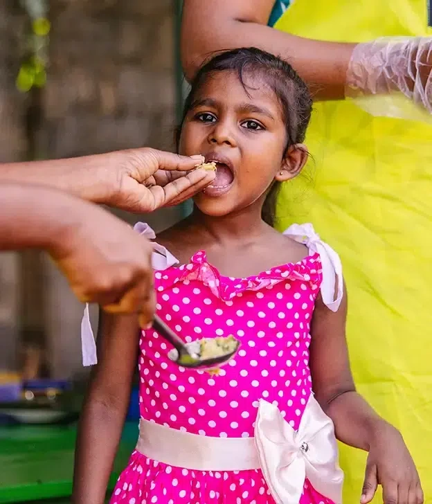 A girl in a pink polka dot dress, opens her mouth to eat.