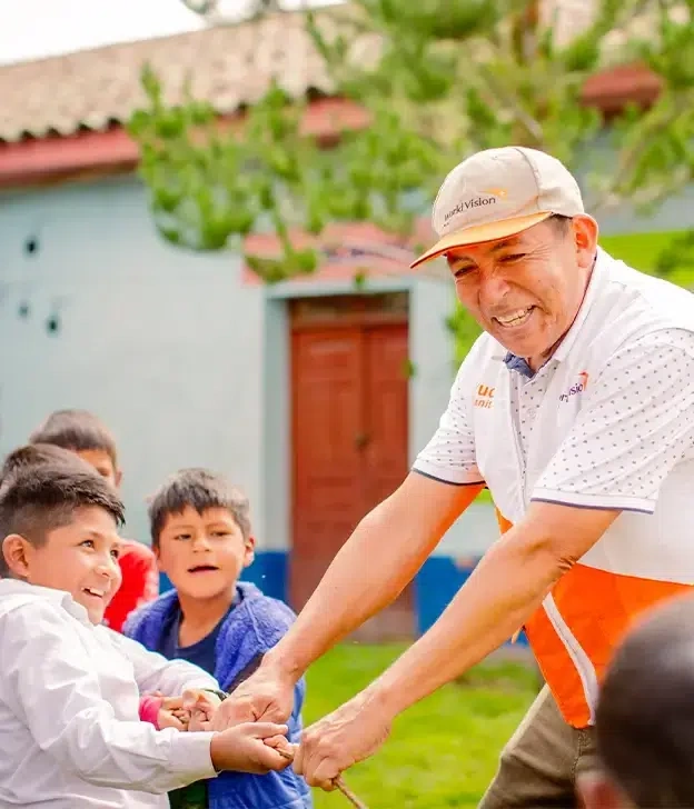 Un garçon et un membre du personnel de World Vision tiennent une corde et jouent au tir à la corde avec d’autres enfants.