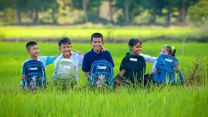 Un groupe de cinq enfants est assis dans l'herbe, un sac à dos à la main.