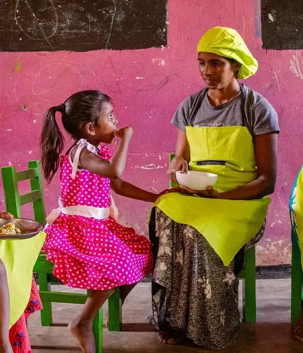 A school girl sits beside a woman as they share a school meal.