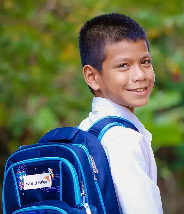A boy turns and smiles while wearing a school backpack.
