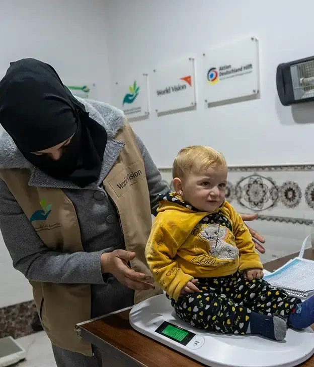 A toddler is weighed on a scale by a World Vision healthcare worker in a clinic.