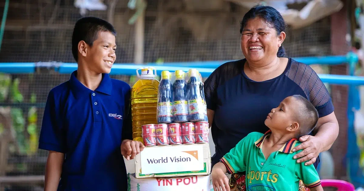 A mother and her two sons smile and stand around a pile of packaged food.