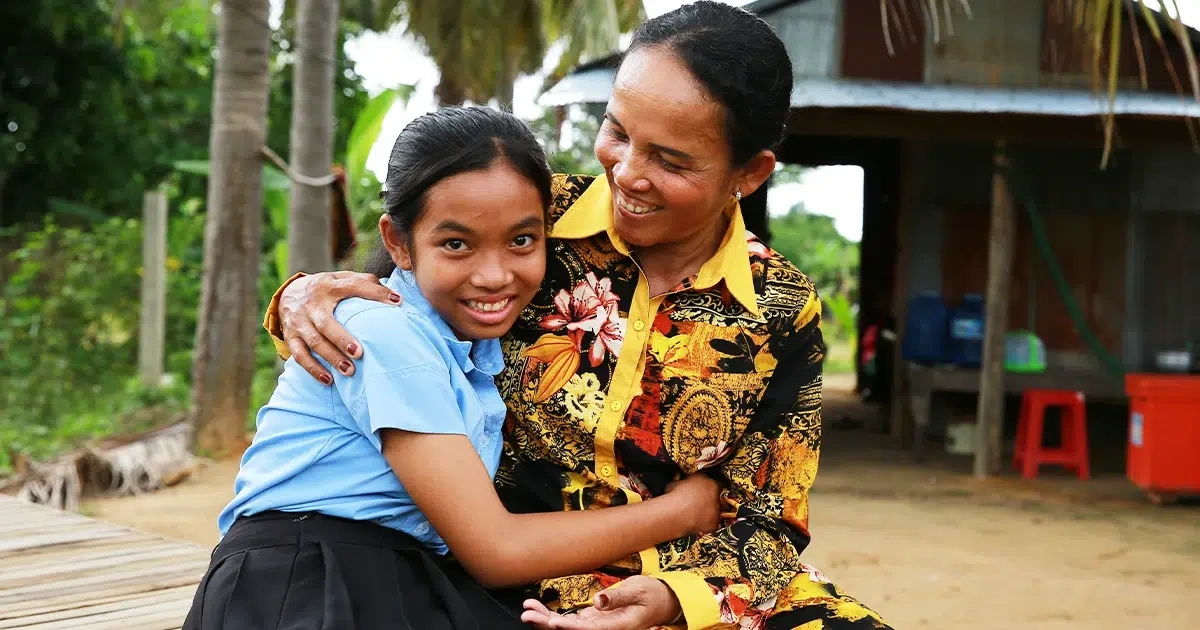 A girl in a blue collared shirt, hugs the woman sitting beside her.