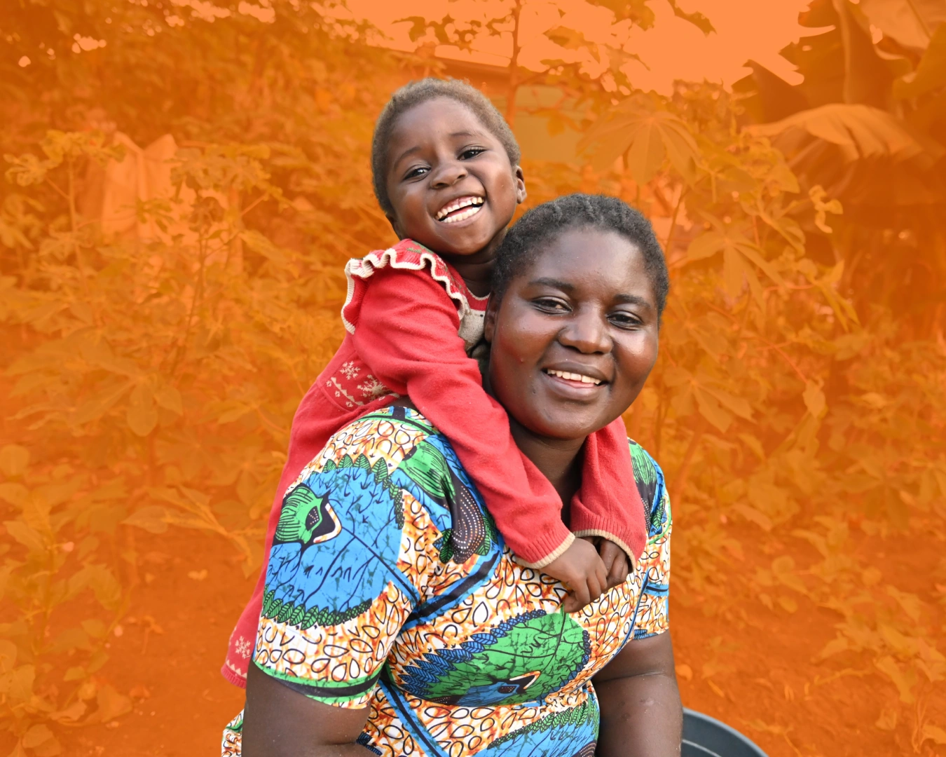 A mother carries her daughter on her back as they both smile joyfully at the camera.