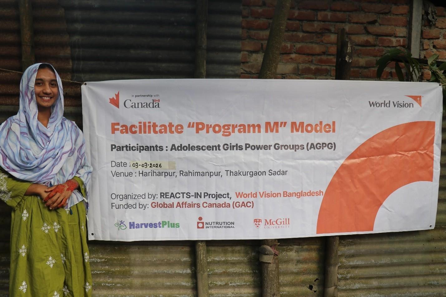 A girl stands beside a banner for the REACTS-IN project.