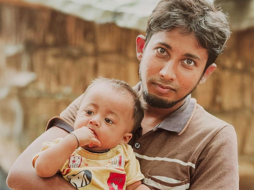 In Bangladesh, a young father makes eye contact while holding his infant.