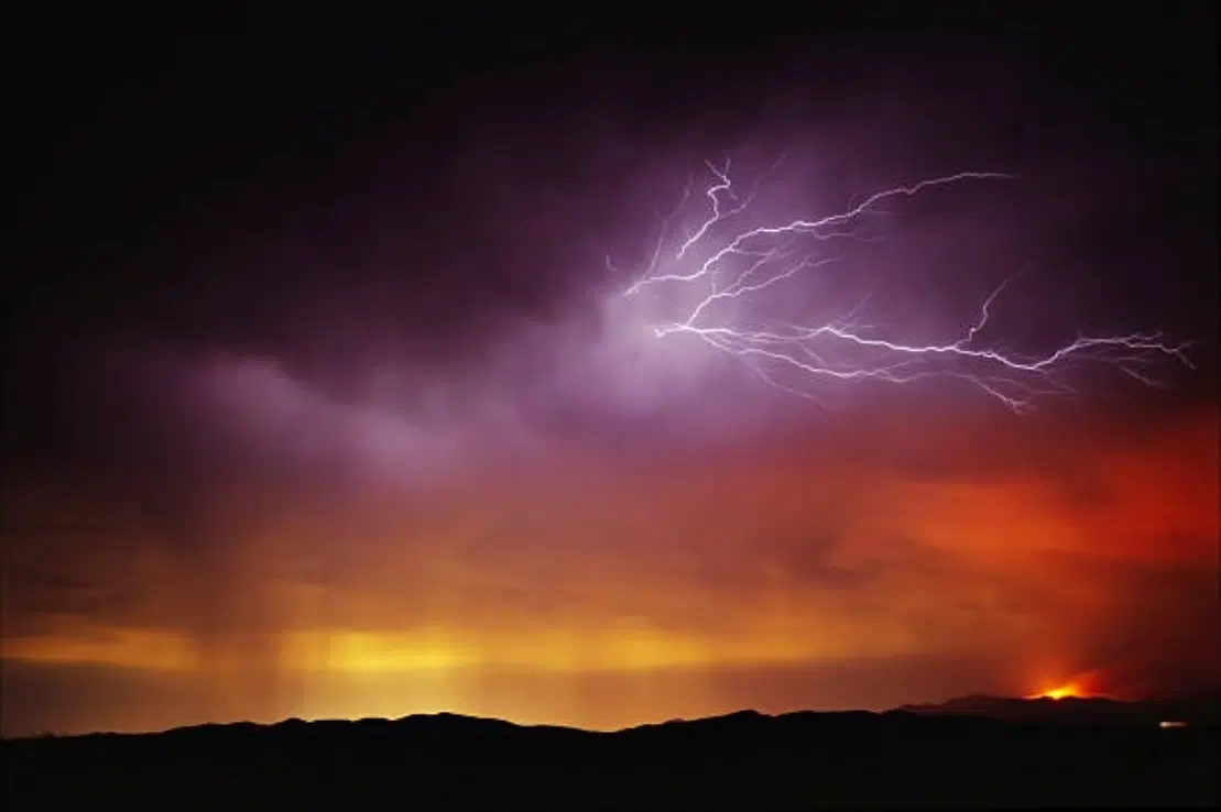 Lightning flashing over the sky while a fire burns below.