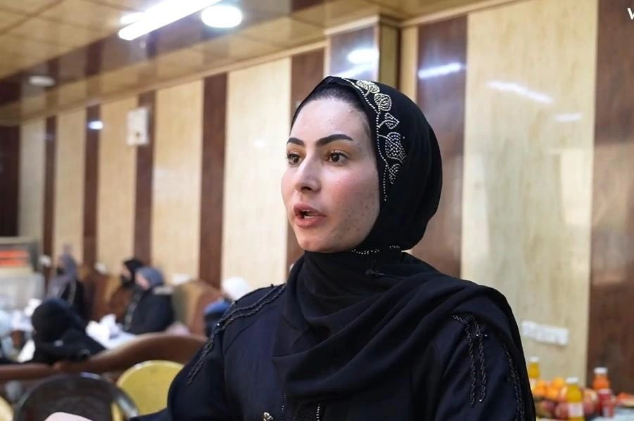 A young woman wearing a headscarf speaks to someone just off camera while standing in the classroom.