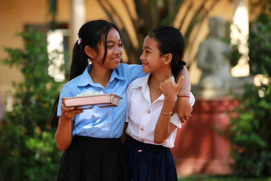 Chandy, holding a meal tray, laughs with a friend outside their school.