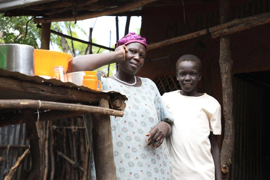 A boy smiles while standing with his mother in their home. 