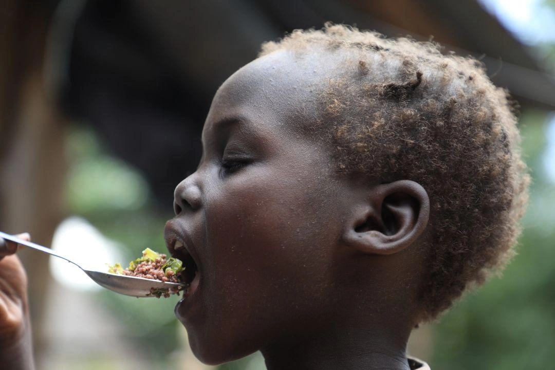 A young child taking a bite of food that his mother made from food items received through World Food Programme and World Vision.