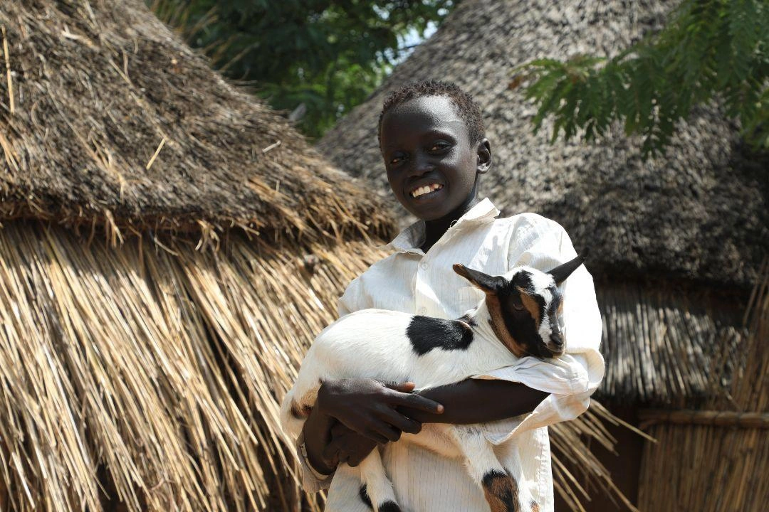 A young boy smiles while holding his little goat. 