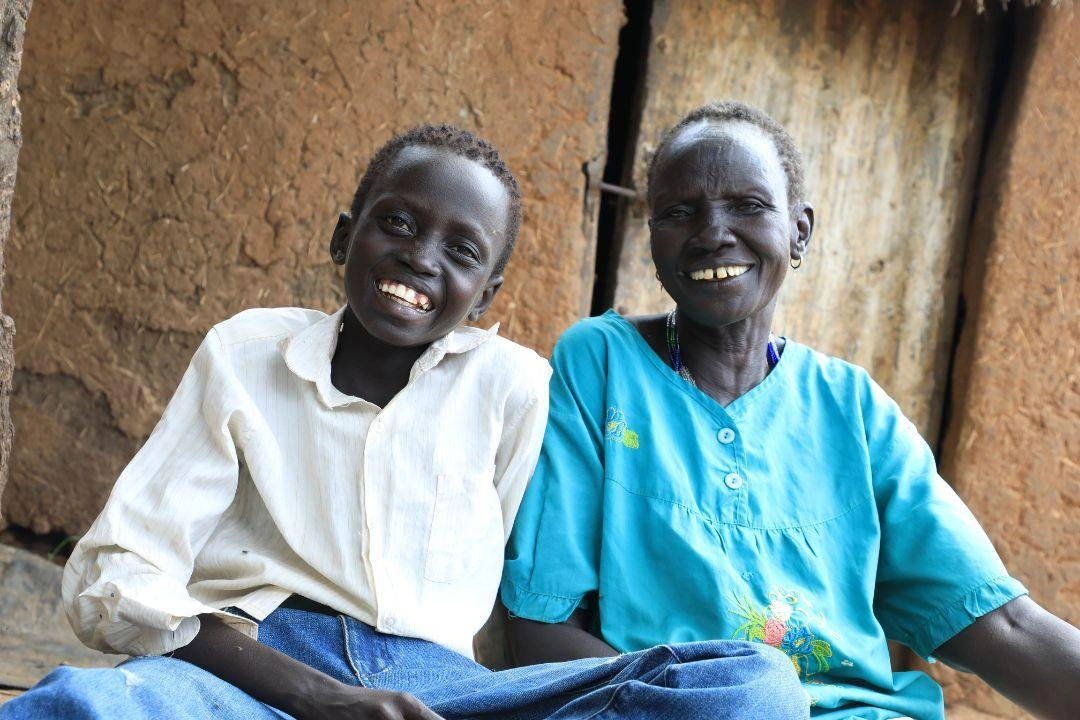 A boy and his grandmother smile together outside their home.