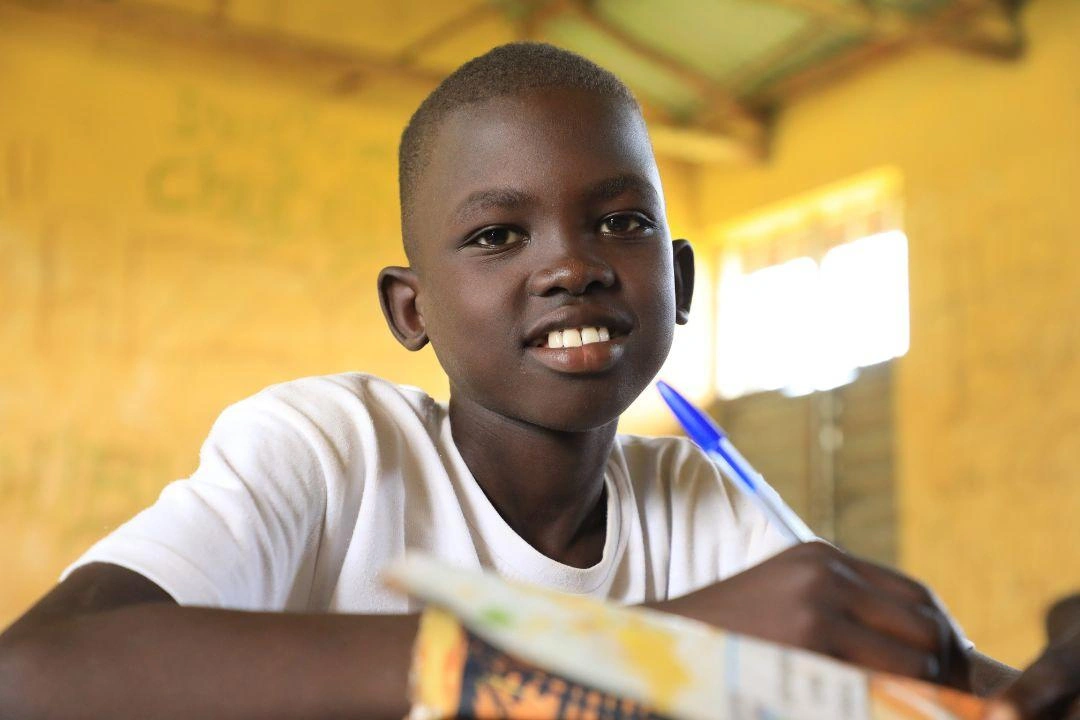 A young boy smiles while sitting in his classroom.